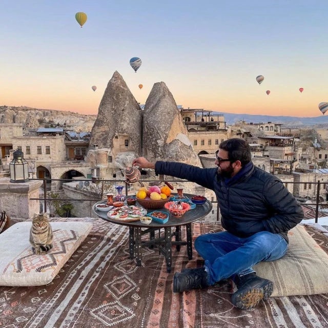 man enjoying a rooftop picnic on a terrace overlooking a sky dotted with hot air balloons