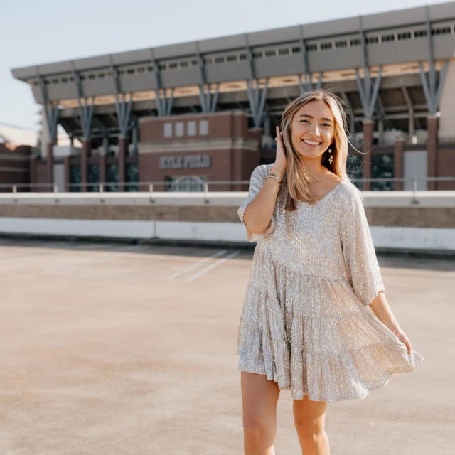 Travel Advisor Allana Webb wears a flowy white dress standing in front of a sports stadium