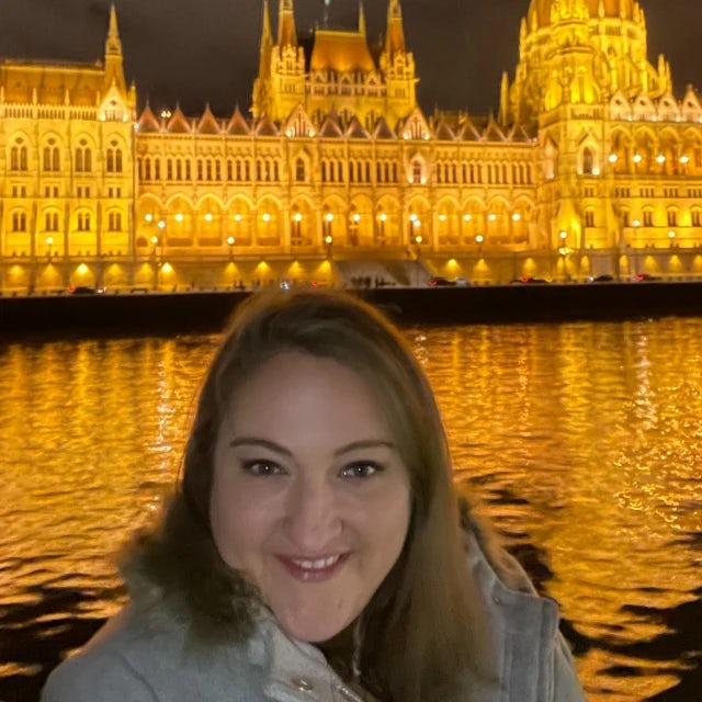 Travel Advisor Meg Lake smiles in front of a castle on the water brightly lit up by golden light