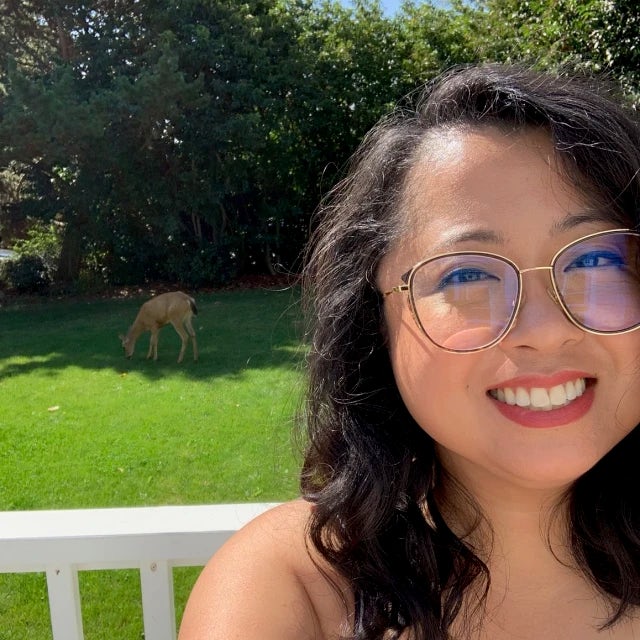 Travel advisor Jennyl Calugas wears a striped navy and blue top and smiles in front of a backyard with a dog in the grass