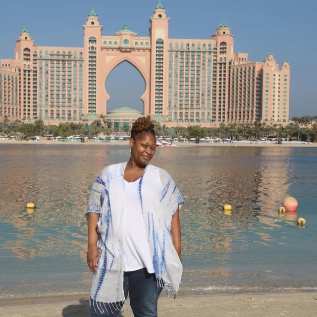 Fora travel agent Djoy Hassan wearing blue shirt and jeans standing in front of Atlantis in the Bahamas