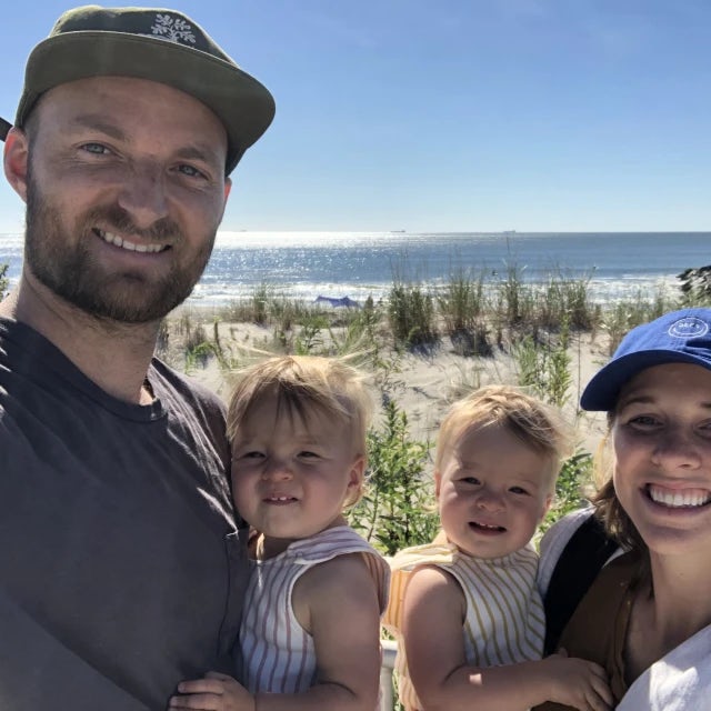 Eric Schultz Fora Travel Agent wearing green hat and grey shirt standing in front of the ocean with his wife and two young daughters.