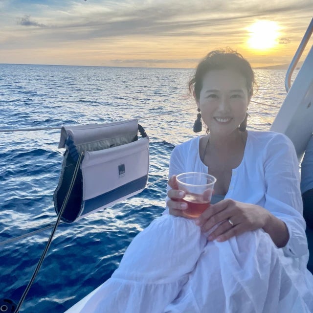 Jini Cho wearing white dress and holding drink in front of the sunset