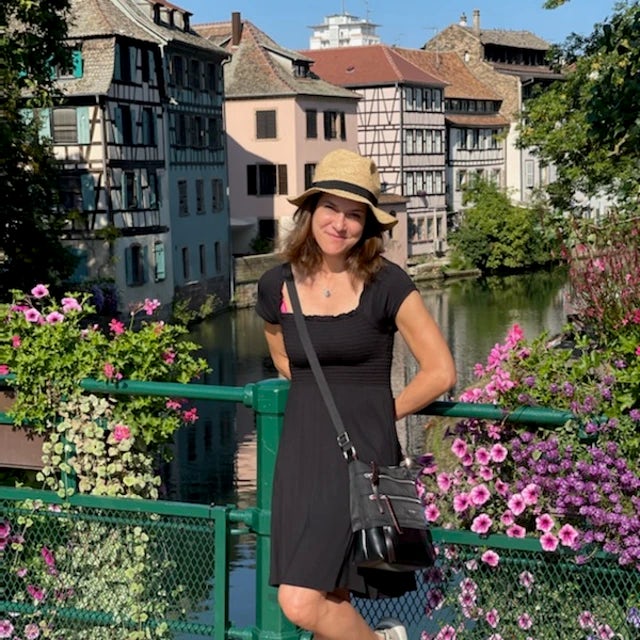 Fora travel agent Lisa Kaplanluzzolino standing by green raining and purple flowers