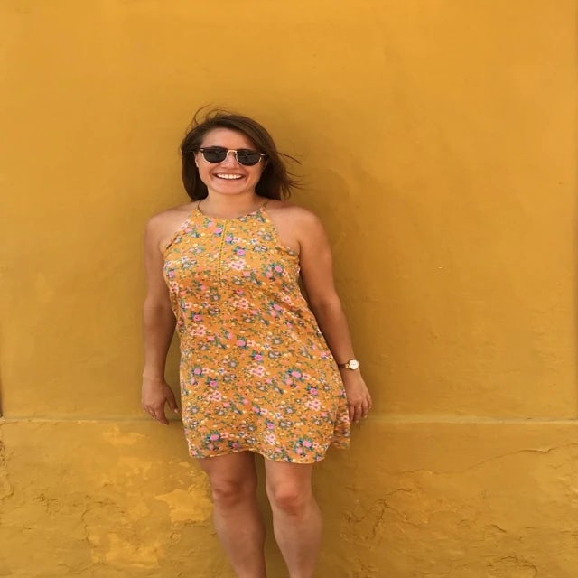 Travel advisor avery laberge wears a yellow dress and stands in front of a yellow wall