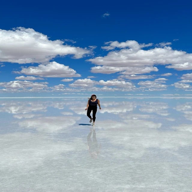 Travel Advisor Logan Hitchcock stands in shallow water with blue sky and clouds reflecting perfectly into the water