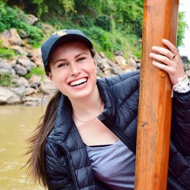 Travel Advisor Emily Richardson in a black jacket and a navy blue hat on a river holding a wooden log.
