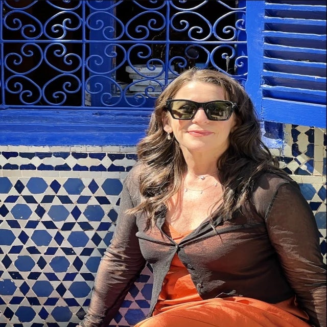 travel advisor Michelle Marx in an orange dress and a black top in front of a blue window