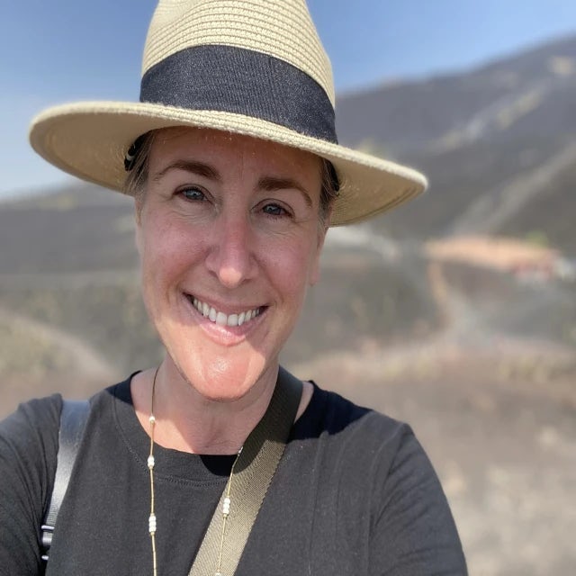 Travel Advisor Lori Loper in a black shirt and tan/black hat in front of the hills.