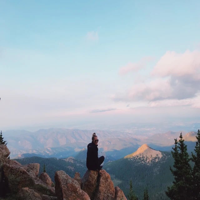 Travel Advisor Shannon Ranzini sitting on a rock at sunset with mountains in the distance.