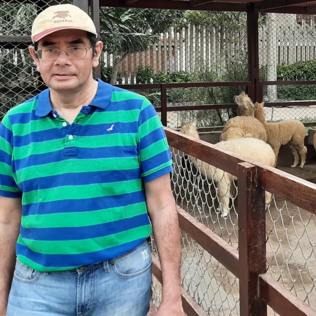 Travel Advisor Sumit Guha in a striped shirt in front of a fence with llamas inside.