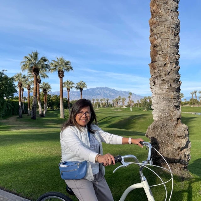 Travel Advisor Gerly Laciste riding a bike with green grass, mountains and palm trees in the distance.