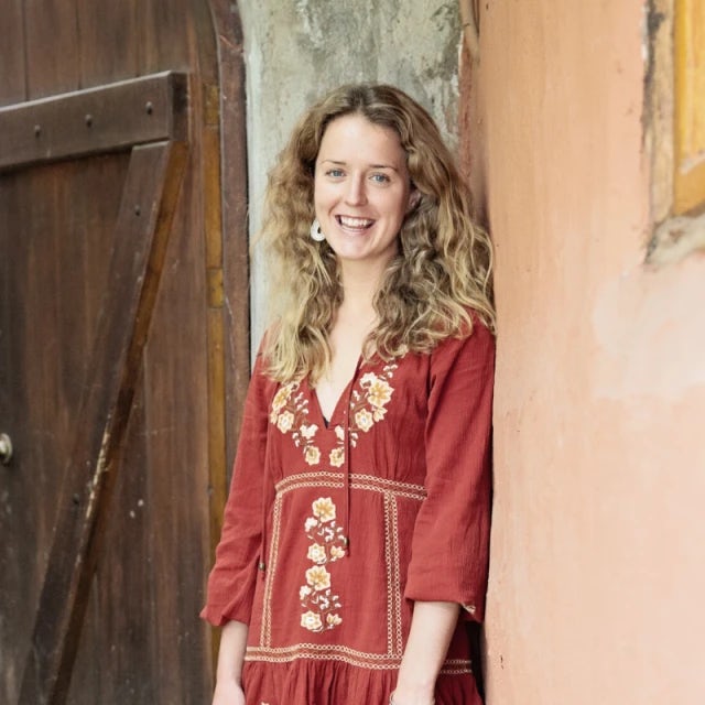 Travel Advisor Veronica Dummett in a red floral dress in front of a beige and wooden wall.