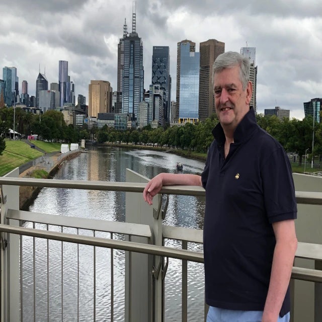 Man smiling in front of buildings and river