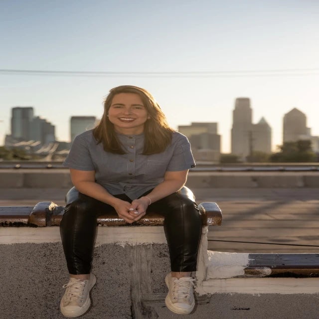Travel Advisor Sharon Payot sitting on a ledge at sunset with a city in the background.