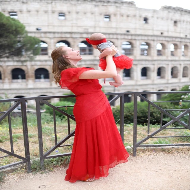 travel advisor Elle Winslow in a red dress holding her baby girl in front of the Colosseum 