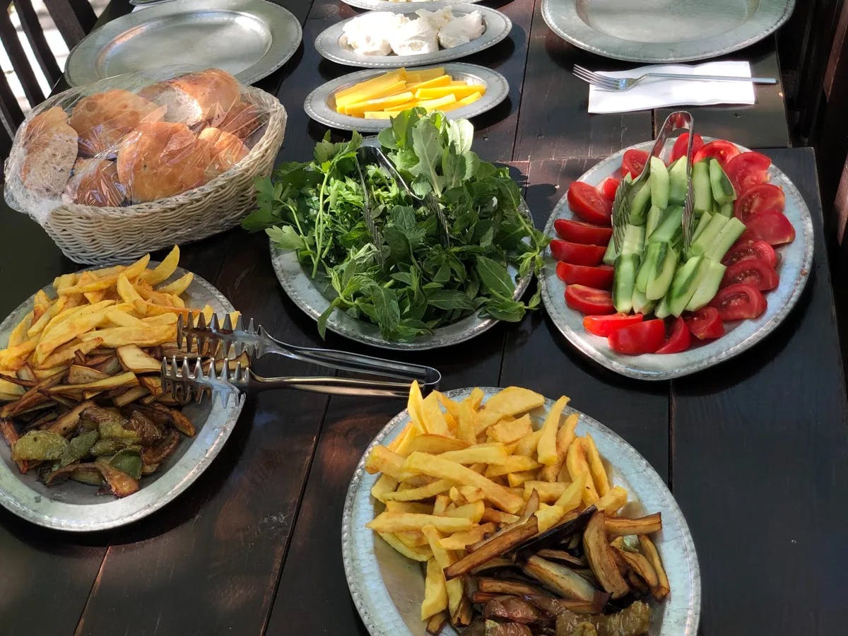 A table full of various food items, such as lettuce, tomatoes, cucumber, french fries and more. 