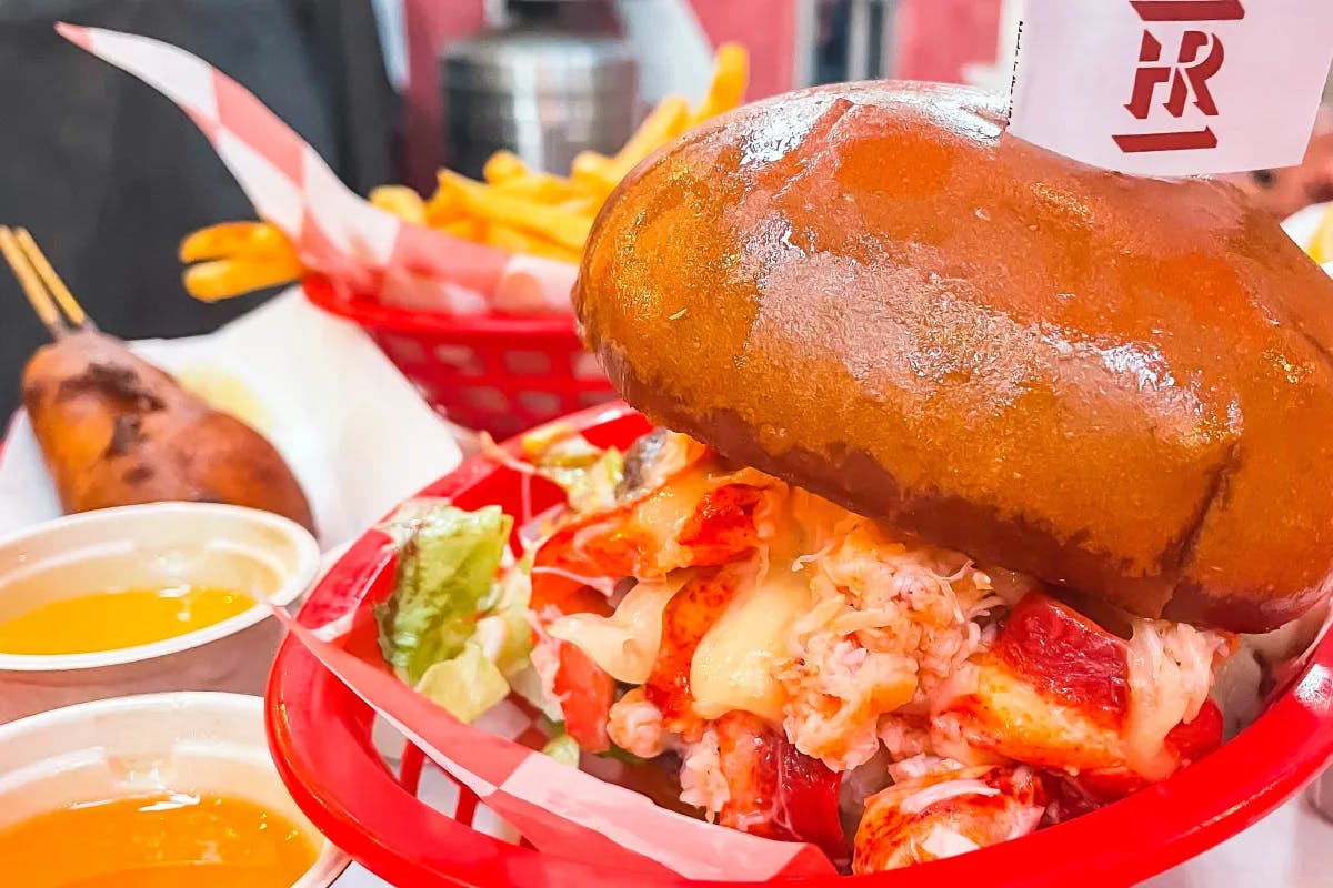 A shiny bun and lobster roll in a red basket with dipping sauces next to it. 