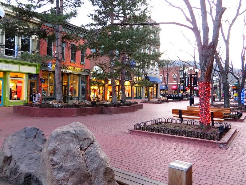 A red brick town square with colorful shops surrounding and trees in planters.