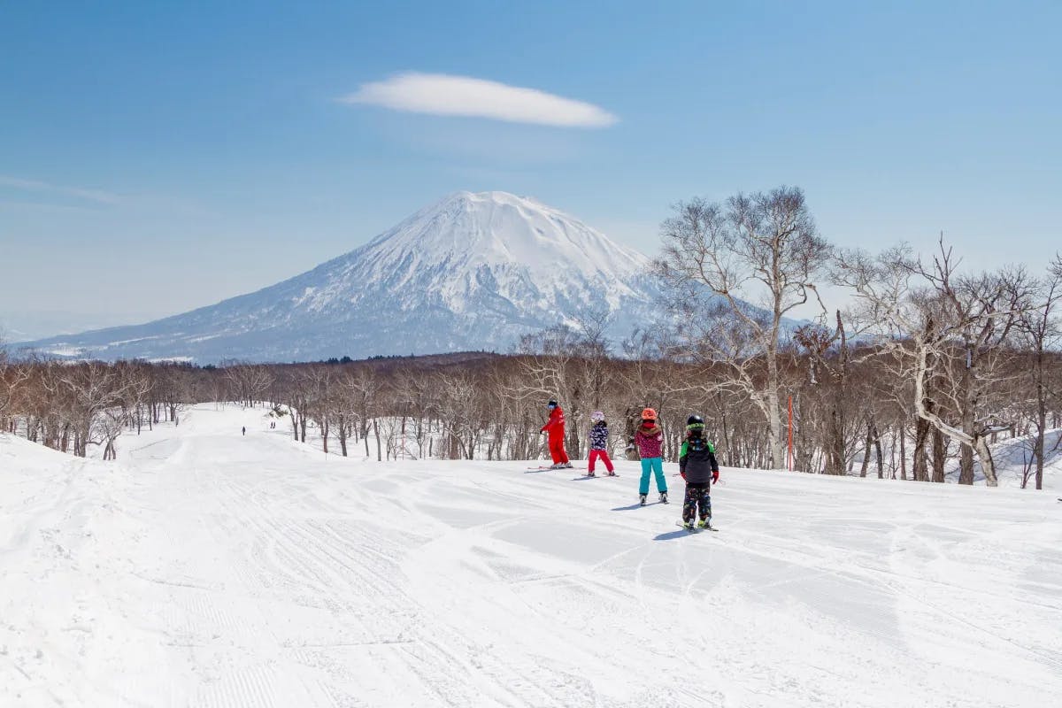 A family skiing at Niseko United with a mountain in the background.