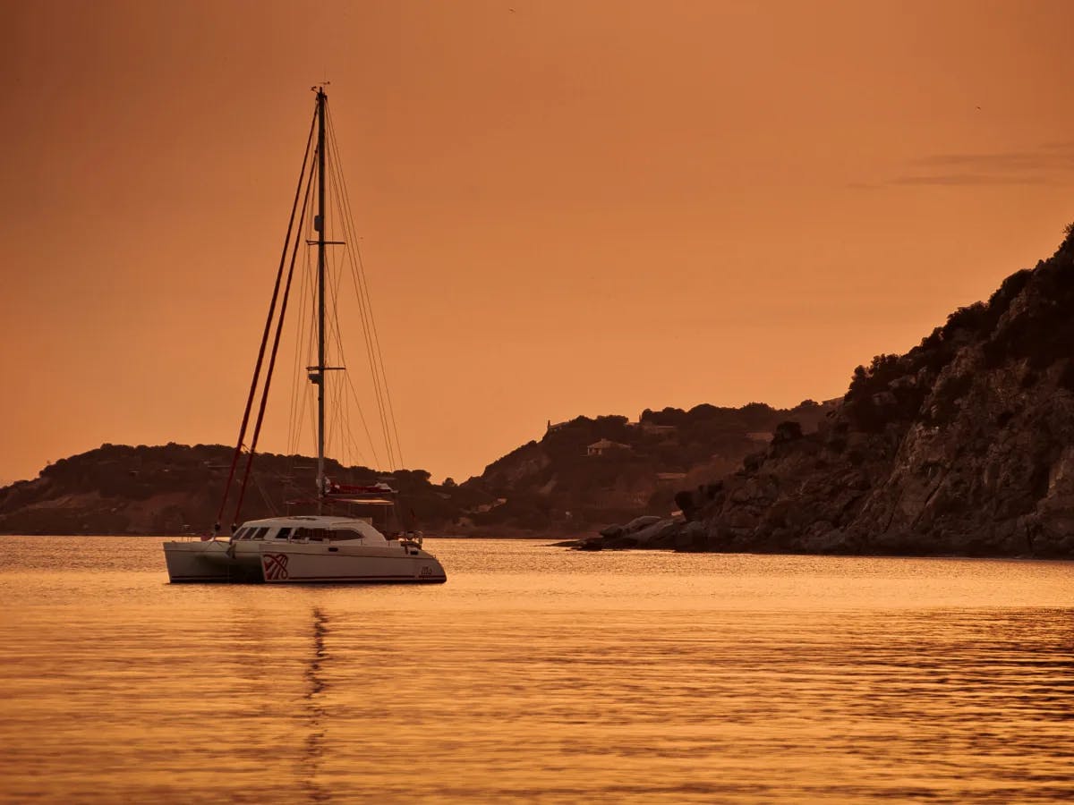 A view of a yacht on the water with a mountain in the background during a golden sunset.