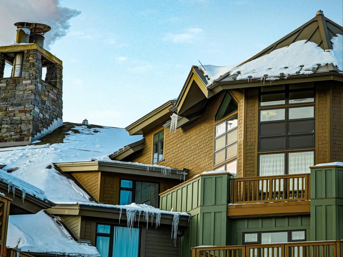 A view of a ski resort exterior complete with wood detailing, green painted paneling and snow covered roofing. 