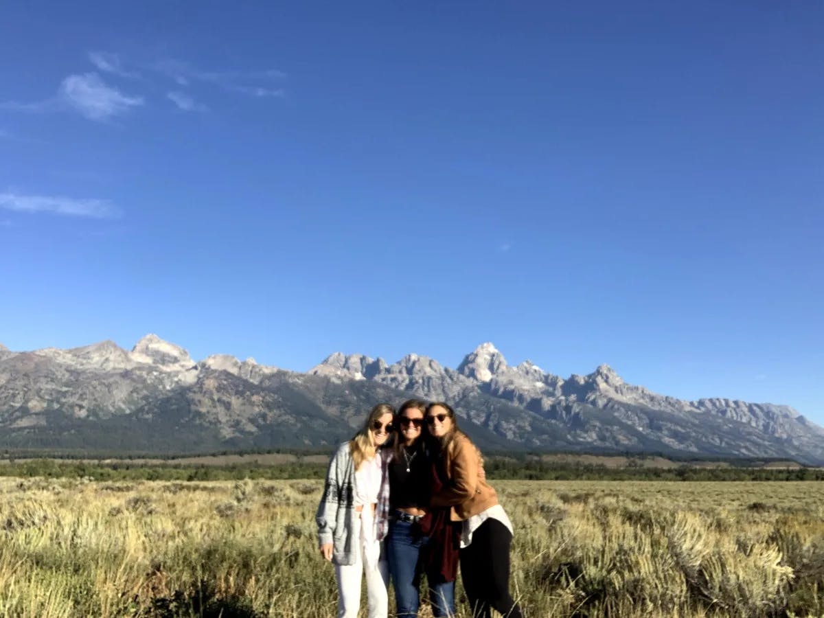 Tori and her friends in sunglasses standing with their arms around each other in front of mountains on a clear day.