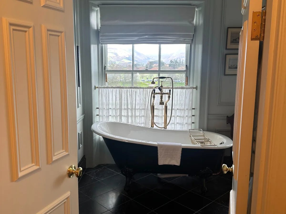 An elegant and old-fashioned style black and white bathtub, with gold-colored faucets, in front a window with white curtains.