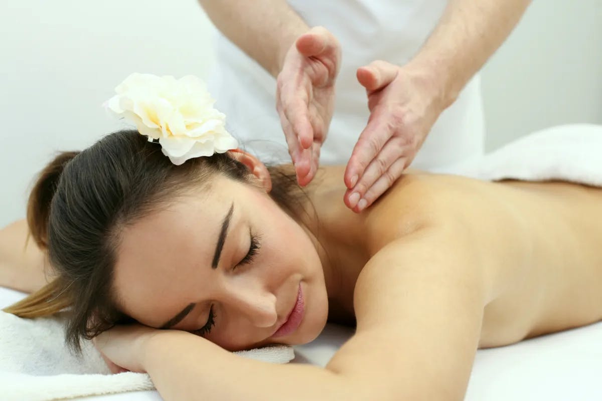 The image depicts a women with a flower in her hair receiving a relaxing massage in a serene setting.
