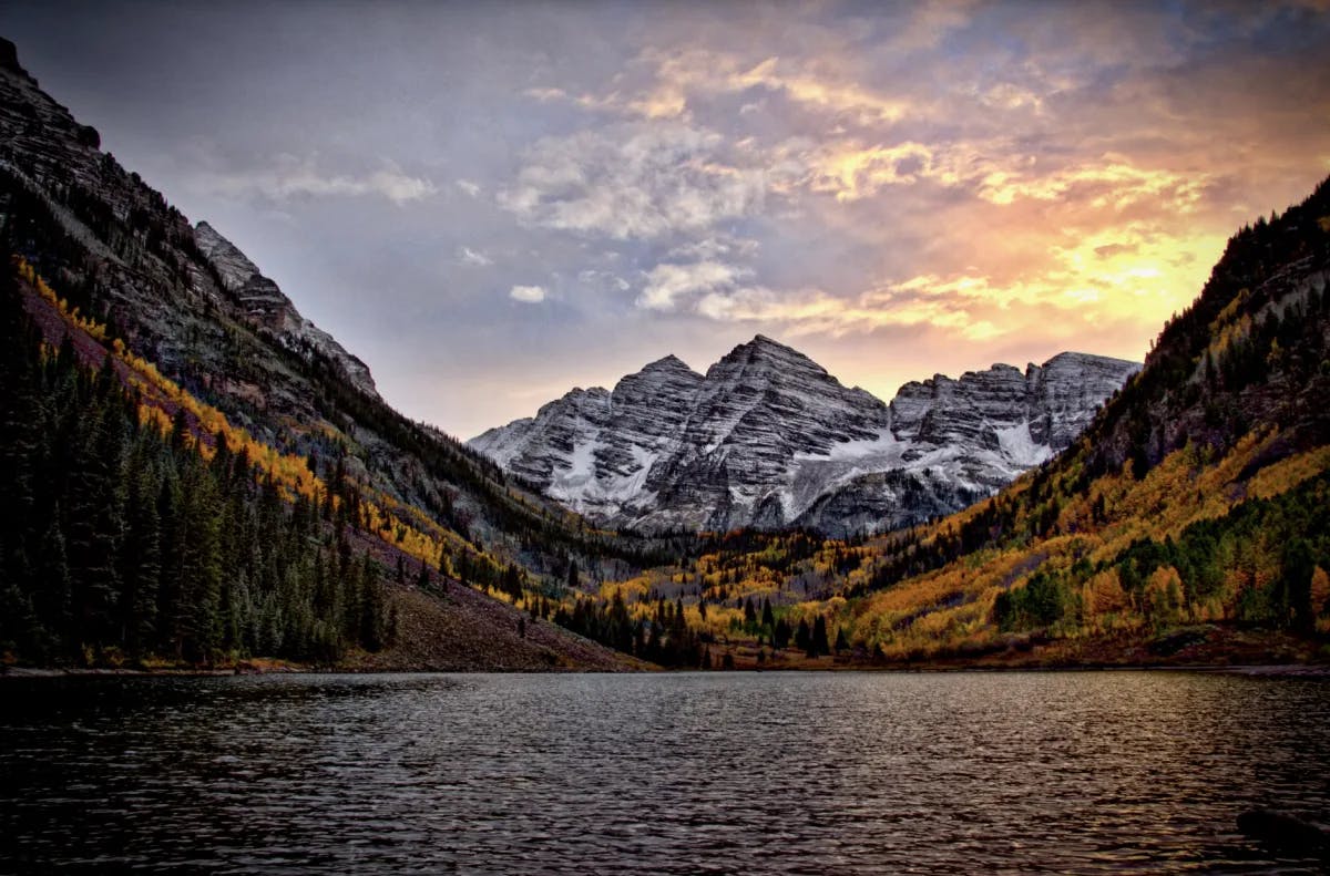 A beautiful lake surrounded by Autumnal trees and a snow covered mountain. 