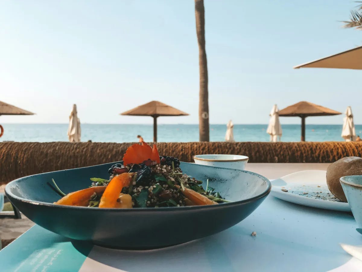 Food served on a black ceramic bowl on a table near a beach with umbrellas