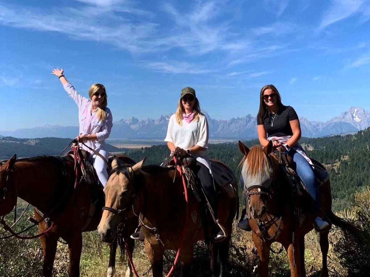 Tori and her friends sitting on horseback in front of a mountain scene.