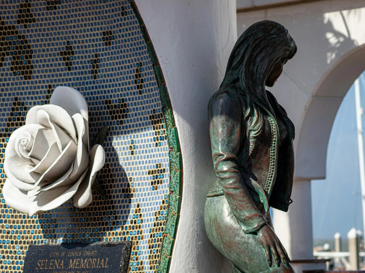 A picture taken in Mirador de la Flor, the Selena Memorial, in Corpus Christi during daytime. It showcases a woman and a large white rose with green and blue tiling. 