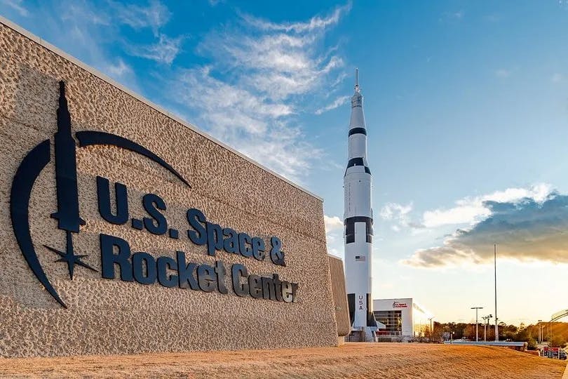 An outdoor sign reading "US Space & Rocket Center" with a rocket in the background during the daytime