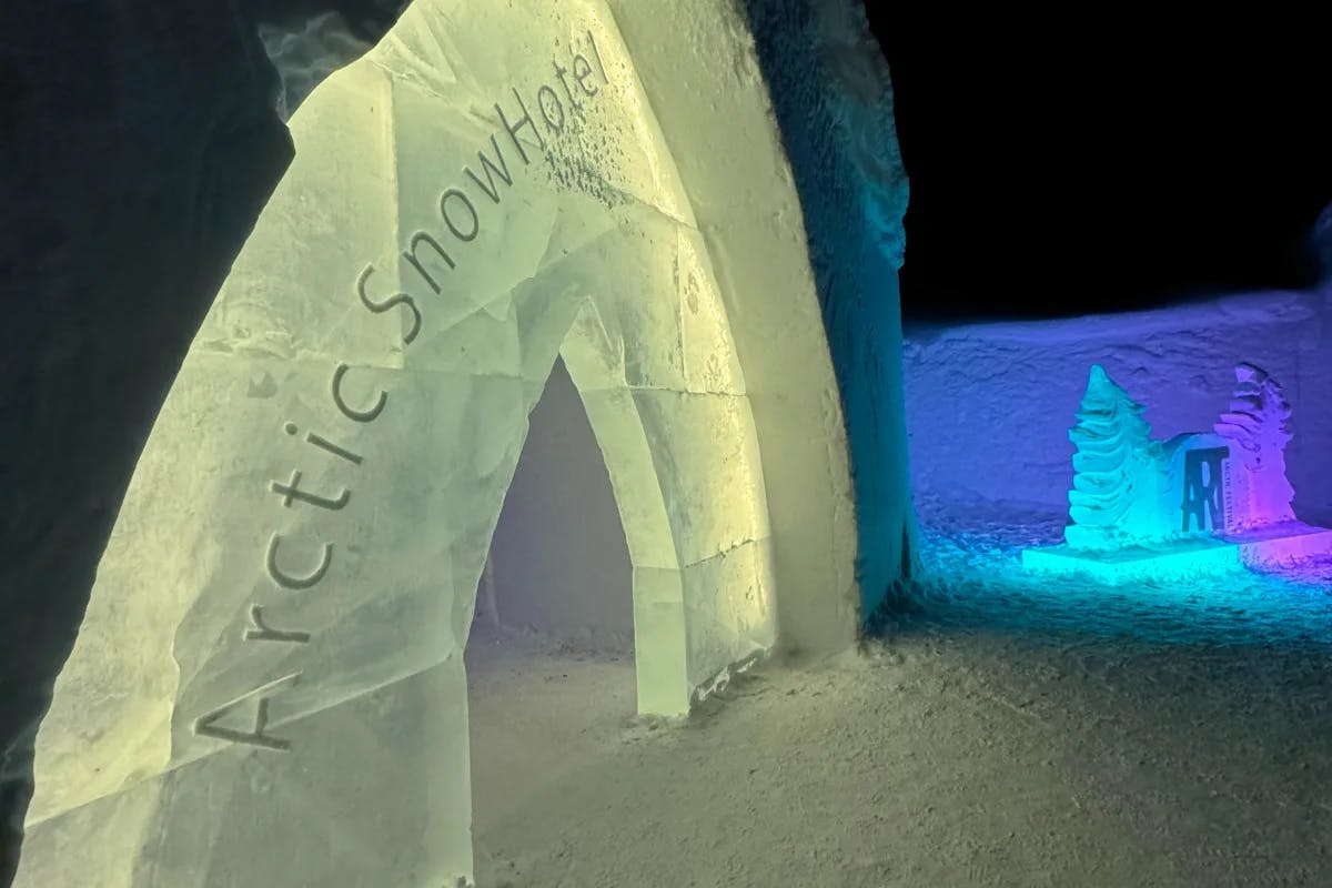 A nighttime view of the entrance to the Arctic Snow Hotel, made of ice, with snow in the background