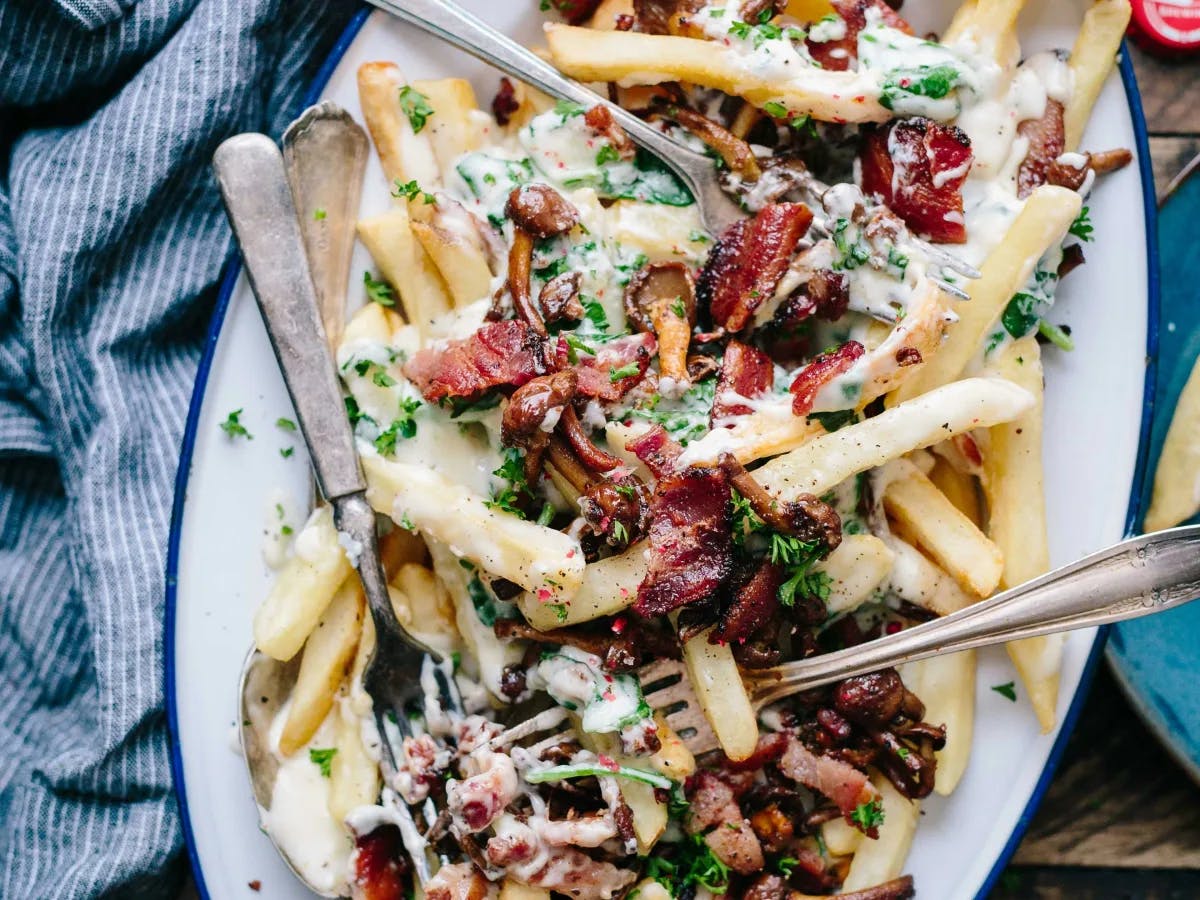 French fries on a plate covered with sauce and bacon 