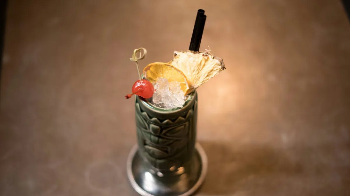A cocktail in a green tiki glass with garnish on top.