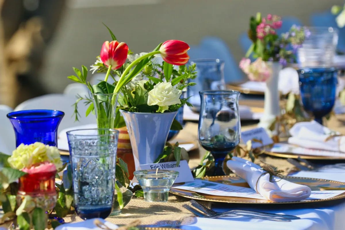 Long table set with red and yellow flowers in vases and blue glasses and gold plates