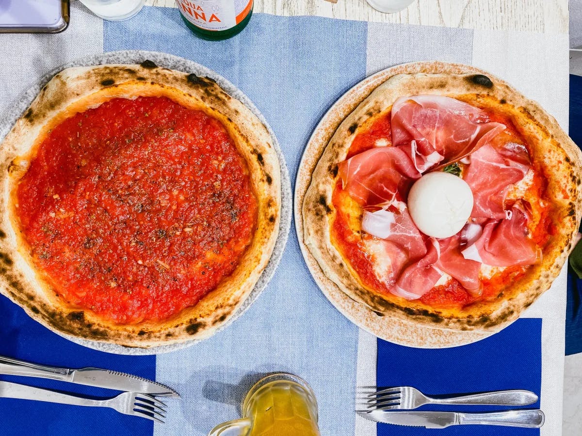 Two pizzas on a blue tablecloth shot from above.