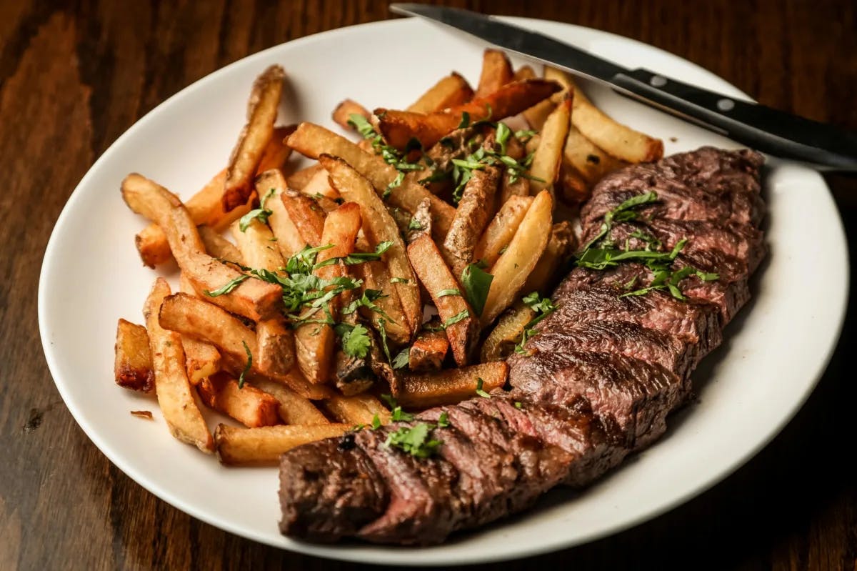 Steak with fries on a white plate on a wooden table.