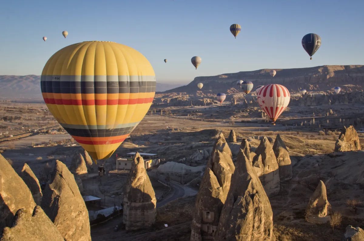 A view of colorful hot air balloons above a desert-like terrain and mountains.
