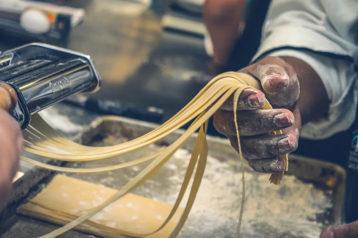 A hand holding dry pasta as it gets pulled out of a pasta making machine. 