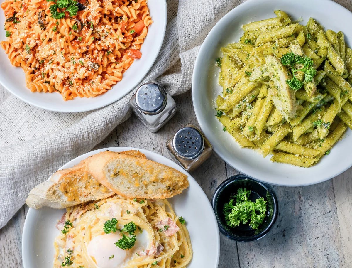 A table with pastas and garlic bread.