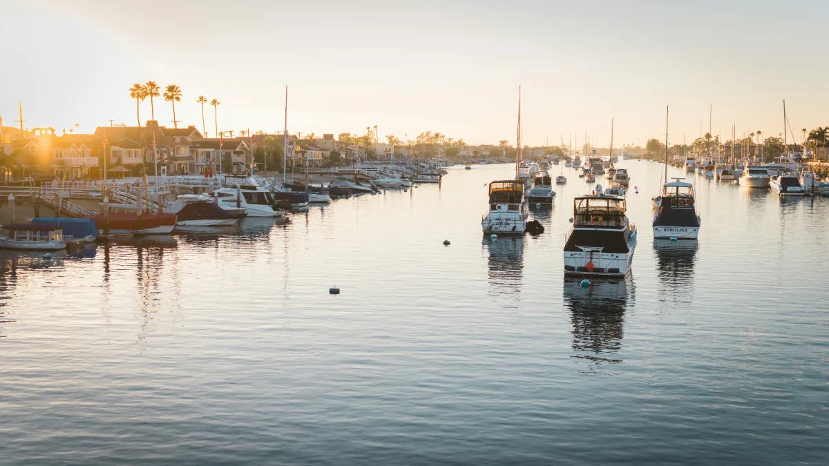 A view of Newport Beach harbor with many yachts docked with the sun low in the sky