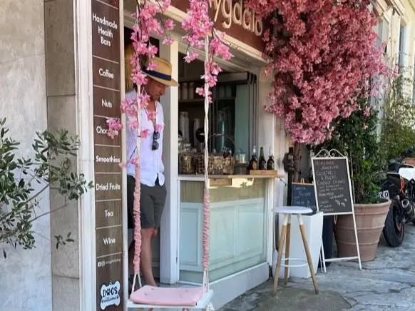 A shop in Athens with pink flowers, a pink swing, a coffee counter and a sign outside.