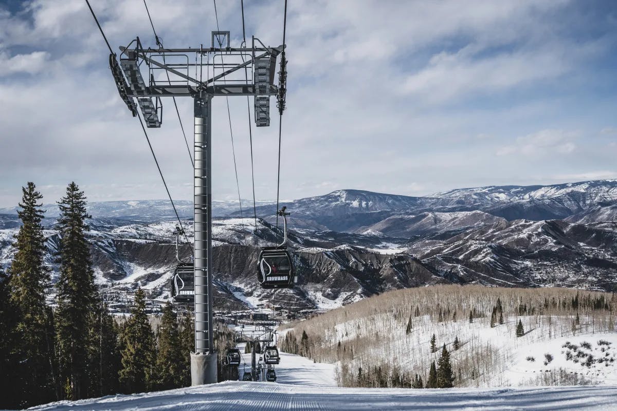 A view of a chair lift, above the slopes, with a view of the snowy mountains of Aspen.