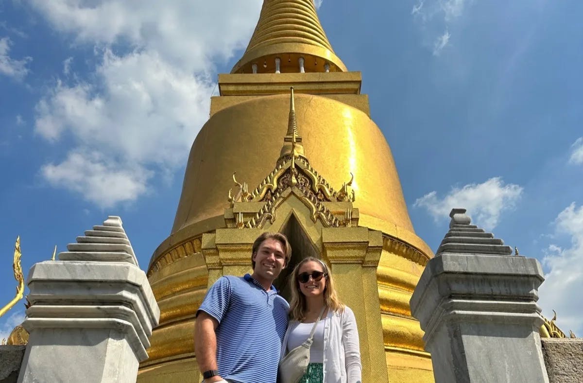 Tori and her partner posing in front of a golden temple on a day with blue skies and spotty clouds.