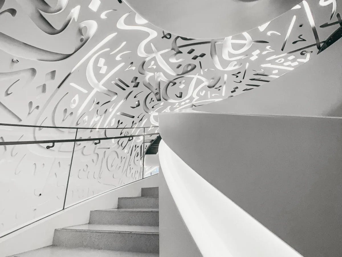 A staircase with white walls with Arabic written on them in silver color.