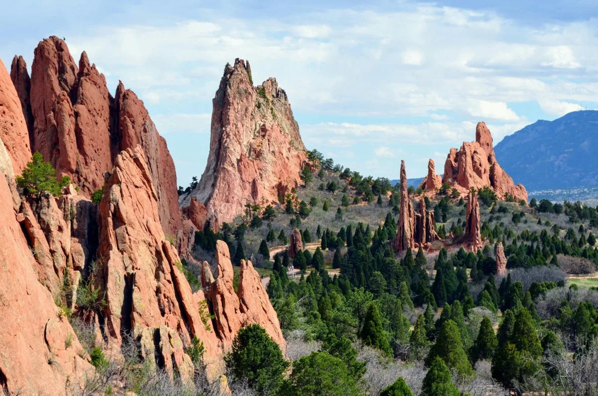 Garden of the Gods, with tall jagged red rocks amidst a landscape of green trees.  