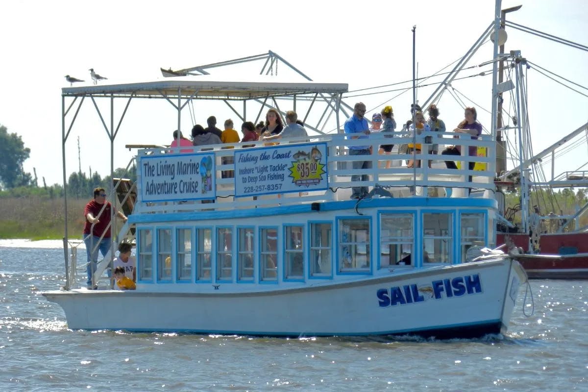 A two-story sailboat with windows that says "Sail Fish" in the water, with people standing on the top deck.